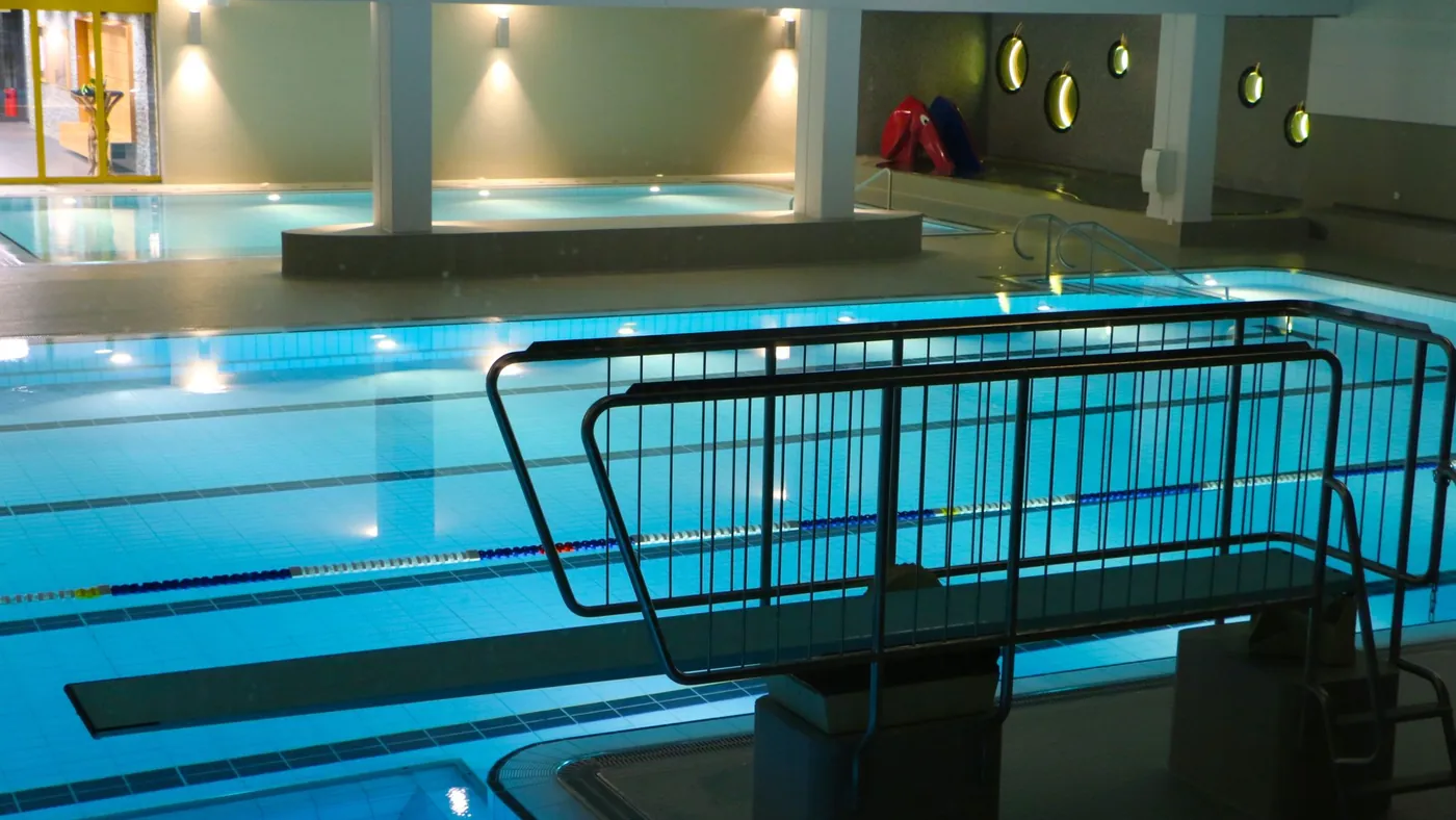 Hallenbad am Abend mit beleuchtetem Becken und Bahnentrennleinen